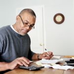 A man working on his finances with a calculator and a pen in hand.